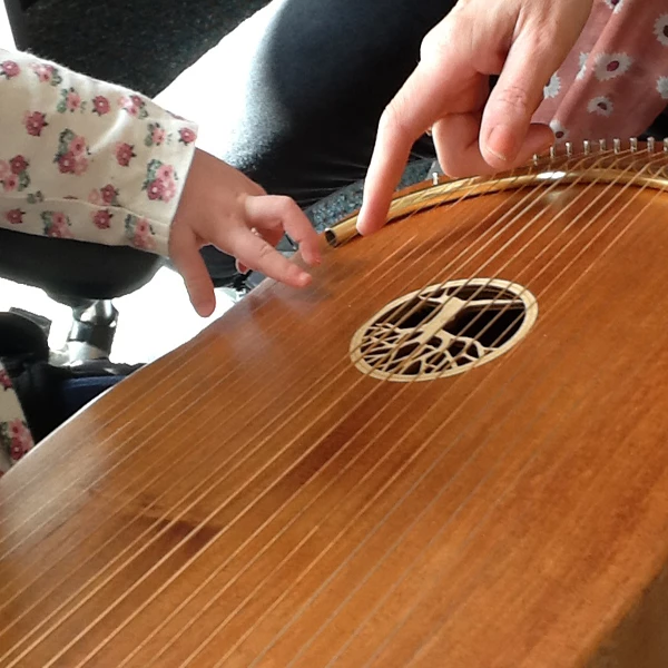 Hands of a young child and a music therapist playing a lyre together