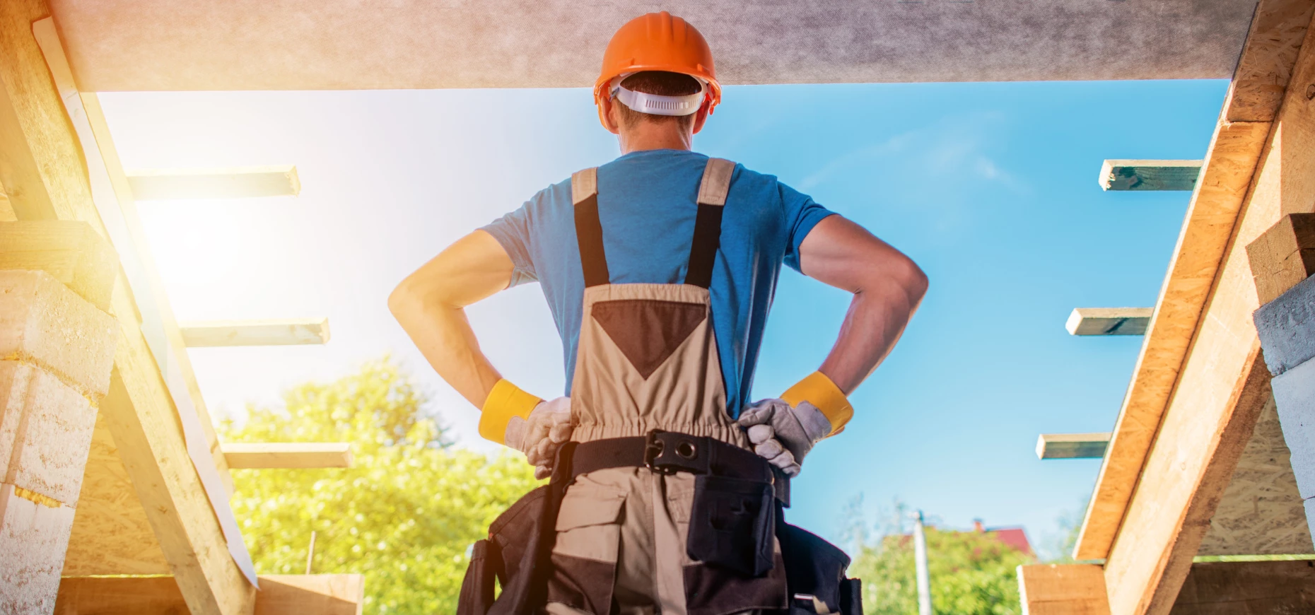 A construction worker wearing a hi-vis jacket and hard hat stands in a house currently under construction.