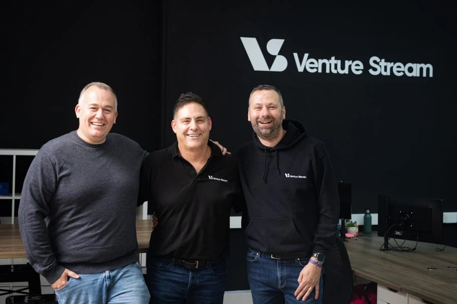 Venture Stream’s chief operating officer Andy Robinson, chief executive officer Vic Morgan, and chief commercial officer James Chapman stand in front of a black wall with the 'Venture Stream' logo in white