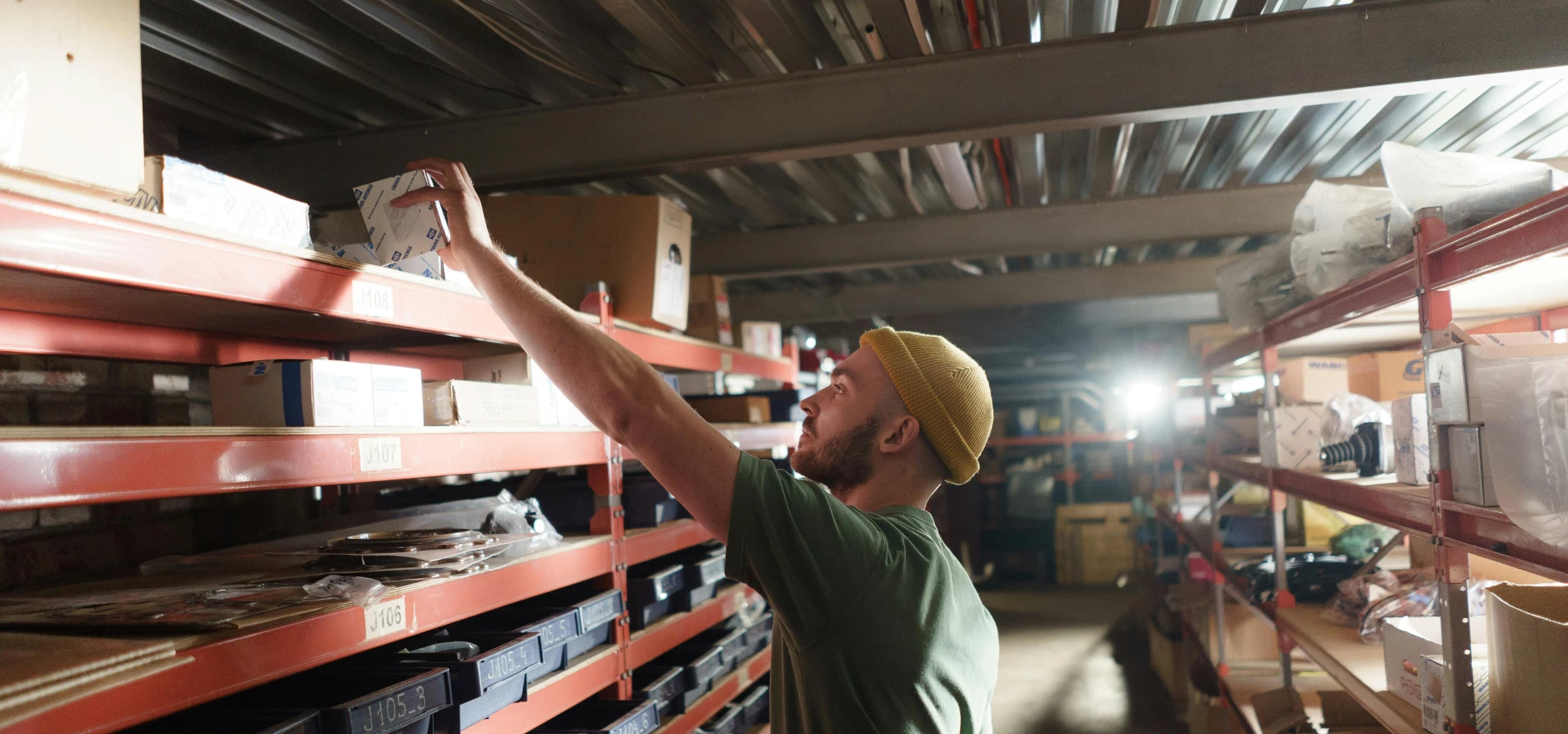 Man in Knit Hat Holding a Small Box in Storeroom