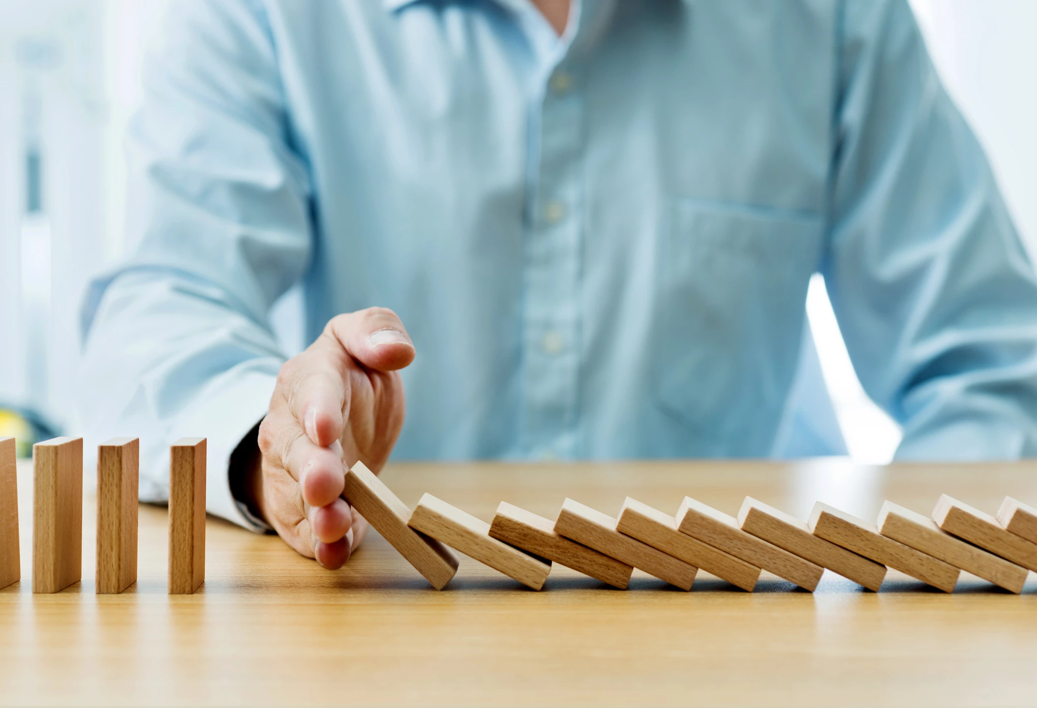 Businessman hand stopping falling blocks on table.